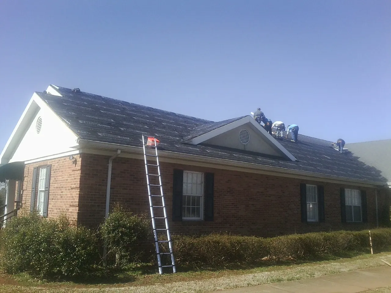 Crew tearing shingles off a brick ranch roof with a ladder set — Emergency Roof Repair work by our crew in Waseca