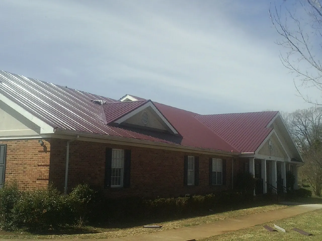 Red metal roof with gabled entries on a long brick building, from a Hail Damage Roof Repair job in Waseca