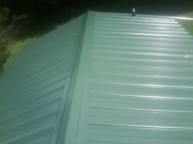 New green metal panels meeting at the ridge of a roof — Flat Roof Repair work by our crew in Waseca