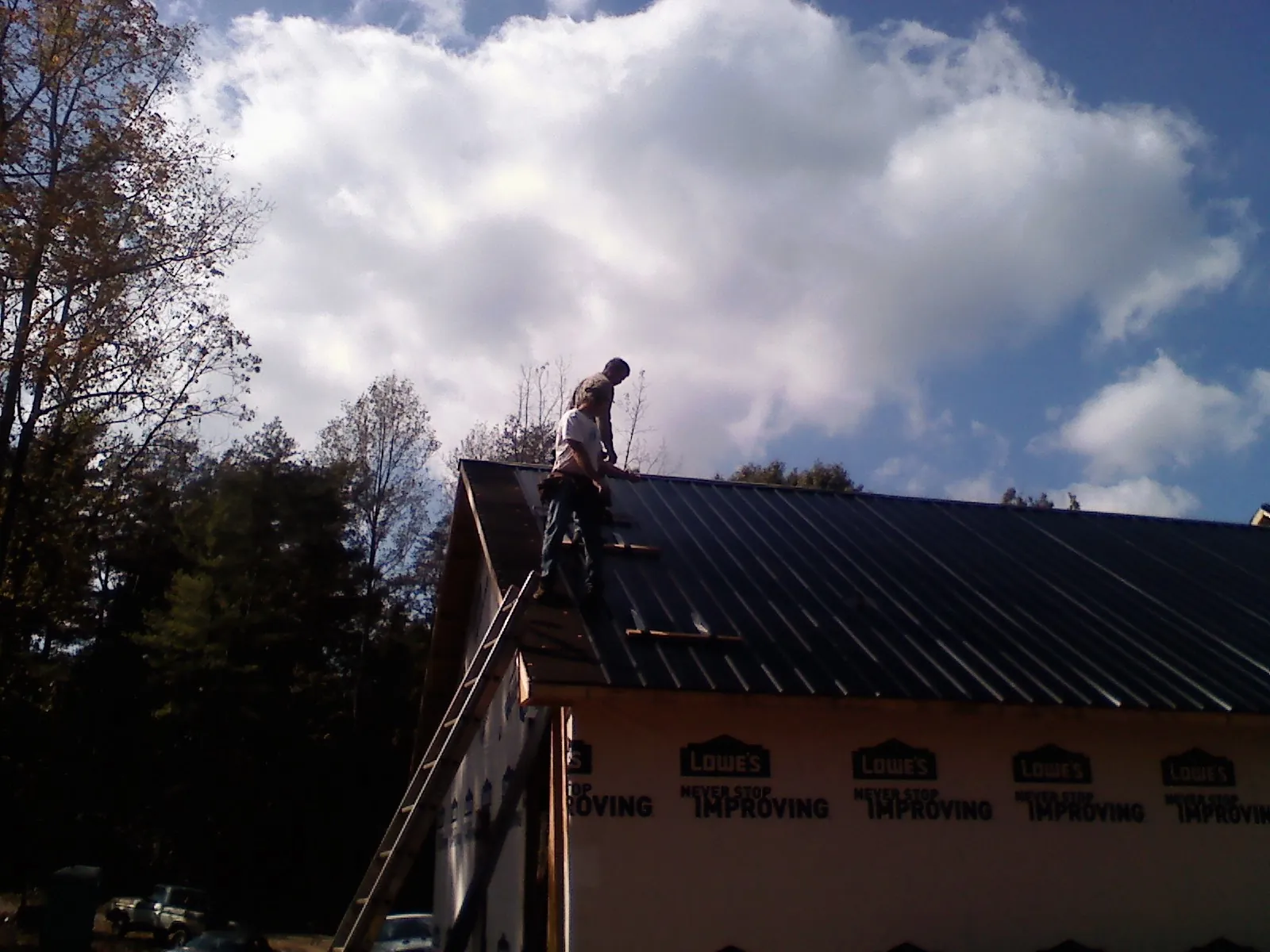 Roofer fastening dark metal panels high against a cloudy sky, from a Roof Inspection job in Waseca